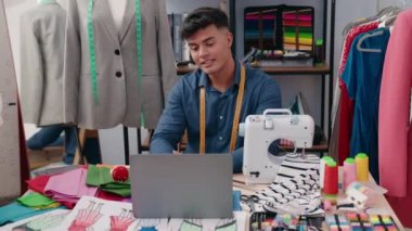 Young hispanic man tailor smiling confident having video call at clothing factory
