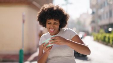 Genç Afro-Amerikalı kadın gülerek sokakta video oyunu oynuyor.