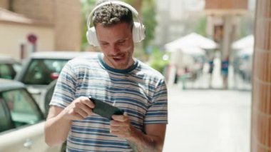 Young hispanic man smiling confident playing video game at street