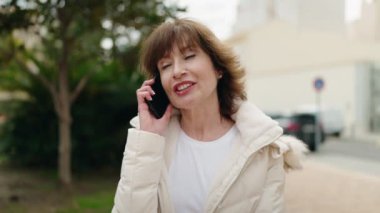 Orta yaşlı bir kadın gülümsüyor. Parktaki akıllı telefondan konuşuyor.