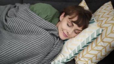 Young caucasian woman sleeping on the sofa covered with blanket at home