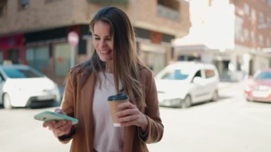 Beyaz kadın akıllı telefon kullanıyor. Sokakta kahve içiyor.