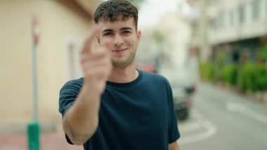 Young hispanic man smiling confident doing coming gesture with hand at street
