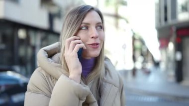 Genç sarışın kadın gülümsüyor. Kendine güveni tam. Akıllı telefondan konuşuyor.
