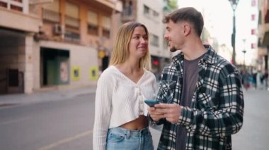 Genç çift sokakta akıllı telefonun yanında kendinden emin bir şekilde selfie çekiyor.