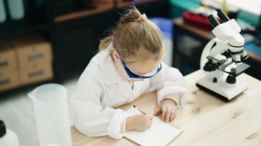 Laboratuvar sınıfında not defterine yazan sevimli sarışın kız öğrenci.