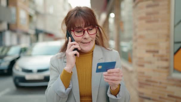 路上でクレジットカードを持っているスマートフォンで話している中年女性のビジネスエグゼクティブ — ストック動画