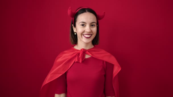 年轻美丽的惊慌失措的女人穿着魔鬼的服装 夹在孤零零的红色背景下的南瓜篮之间 — 图库视频影像