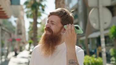 Genç kızıl saçlı adam gülümsüyor. Caddedeki akıllı telefondan kendine güvenen bir sesli mesaj dinliyor.