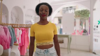 Afro-Amerikan kadın müşteri gülerek elbise dükkanında alışveriş torbaları tutuyor.
