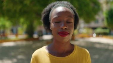 Afro-Amerikalı kadın parkta kendinden emin bir şekilde gülümsüyor.