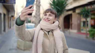 Sokakta akıllı telefonlu genç bir beyaz kadın görüntülü görüşme yapıyor.