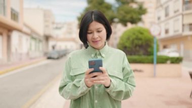 Genç Çinli kadın sokakta akıllı telefon kullanıyor.