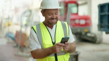 Orta yaşlı bir mimar sokakta akıllı telefon kullanıyor.