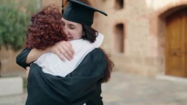 Two women mother and daughter hugging each other celebrating graduation at campus university