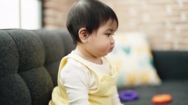 Adorable hispanic baby holding toy sitting on sofa at home