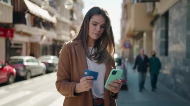 Beyaz bir kadın sokakta akıllı telefon ve kredi kartı kullanıyor.