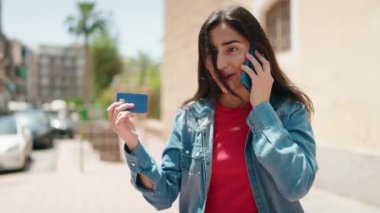 Genç İspanyol kız akıllı telefondan konuşuyor ve sokakta kredi kartı kullanıyor.