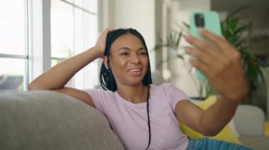 Afro-Amerikalı bir kadın evdeki koltukta video görüşmesi yapıyor.