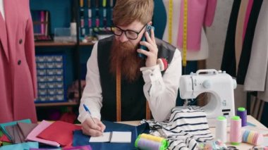 Genç kızıl saçlı terzi akıllı telefondan konuşuyor. Giyim fabrikasında deftere yazı yazıyor.
