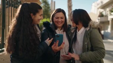 Mother and daughters smiling confident using smartphone at street