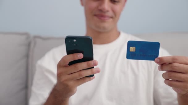 Joven Hombre Hispano Usando Teléfono Inteligente Tarjeta Crédito Sentado Sofá — Vídeo de stock