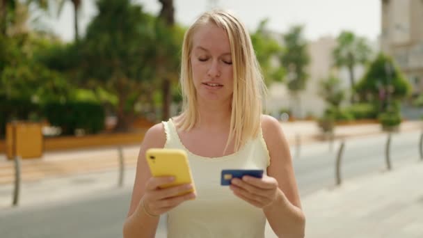 在公园用智能手机和信用卡的年轻金发女人 — 图库视频影像