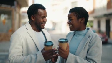 Afro-Amerikalı çift gülerek sokakta kahve içiyor.