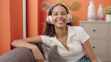 Young african american woman listening to music sitting on sofa at home