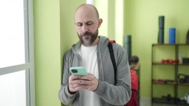 Genç kel adam spor merkezinde akıllı telefon kullanıyor.