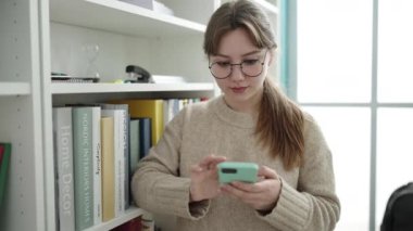 Young blonde woman student using smartphone at library university