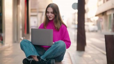 Young blonde woman smiling confident using laptop at street