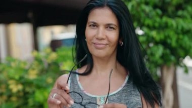 Orta yaşlı İspanyol kadın sokakta kendine güvenen gözlüklü gülümsüyor.