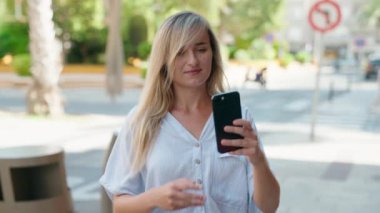 Young blonde woman smiling confident making selfie by the smartphone at street