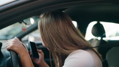 Young woman using smartphone sitting on car at street