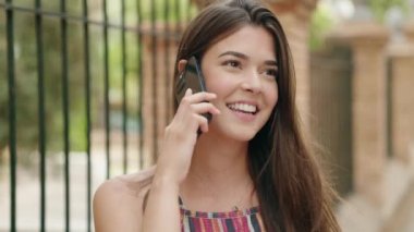Genç, güzel, İspanyol bir kadın gülümsüyor ve caddede akıllı telefondan konuşuyor.