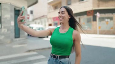 Genç ve güzel İspanyol kadın gülümsüyor. Kendine güveni tam. Sokakta akıllı telefonun yanında selfie çekiyor.