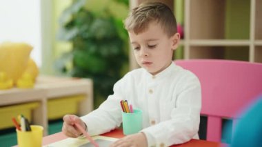 Adorable caucasian boy student sitting on table drawing on paper at kindergarten