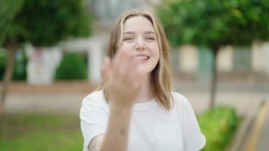 Young caucasian woman smiling confident doing coming gesture with hand at park