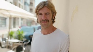 Sokakta kendine güvenen genç sarışın adam gülümsüyor.