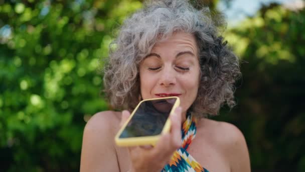 中年白髪の女性は公園でスマートフォンで自信を持って話して笑顔 — ストック動画