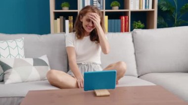Young beautiful hispanic woman watching movie on touchpad sitting on sofa at home