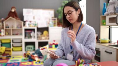 Young beautiful hispanic woman working as a teacher using smartphone at kindergarten