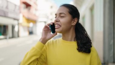 Genç Afrikalı Amerikalı kadın gülümsüyor. Kendine güveni tam. Sokakta akıllı telefondan konuşuyor.