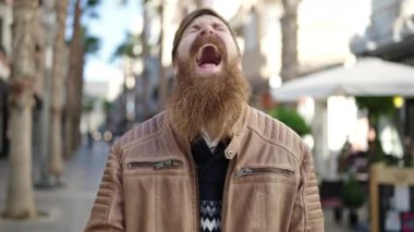 Young redhead man smiling confident pointing with finger at coffee shop terrace