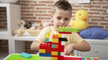 Anaokulundaki masada oturan, inşaat bloklarıyla oynayan sevimli çocuk.