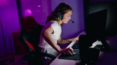 Young beautiful hispanic woman streamer playing video game using computer at gaming room