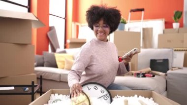 Genç Afrikalı Amerikalı kadın yeni evinde akıllı telefon kullanarak karton kutuları açıyor.