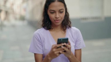 Genç Afro-Amerikalı kadın sokakta akıllı telefon kullanarak gülümsüyor.