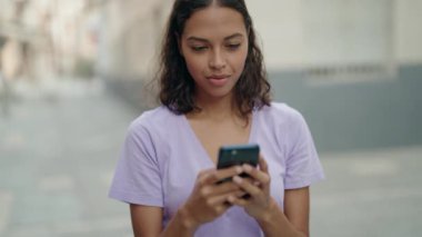 Young african american woman smiling confident using smartphone at street